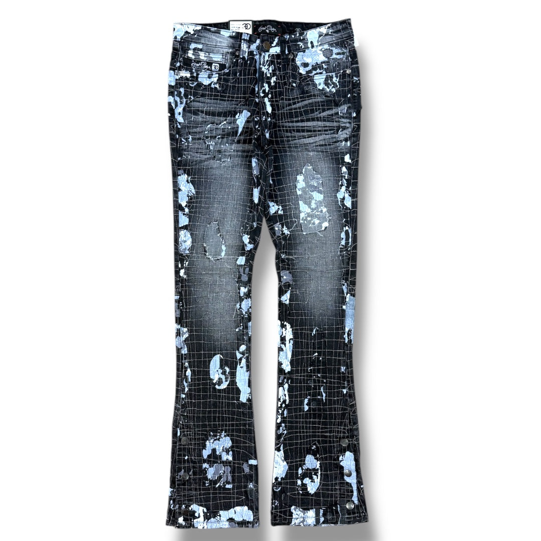 Distressed flare jeans featuring a black and blue grid pattern with abstract splatter and tear details, shown flat against a white background.