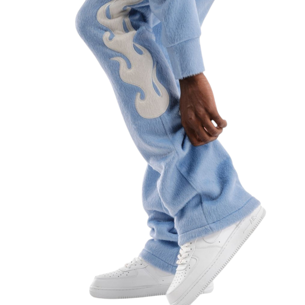 Light blue sweatpants with flame design worn by a person, paired with white sneakers on a white background.
