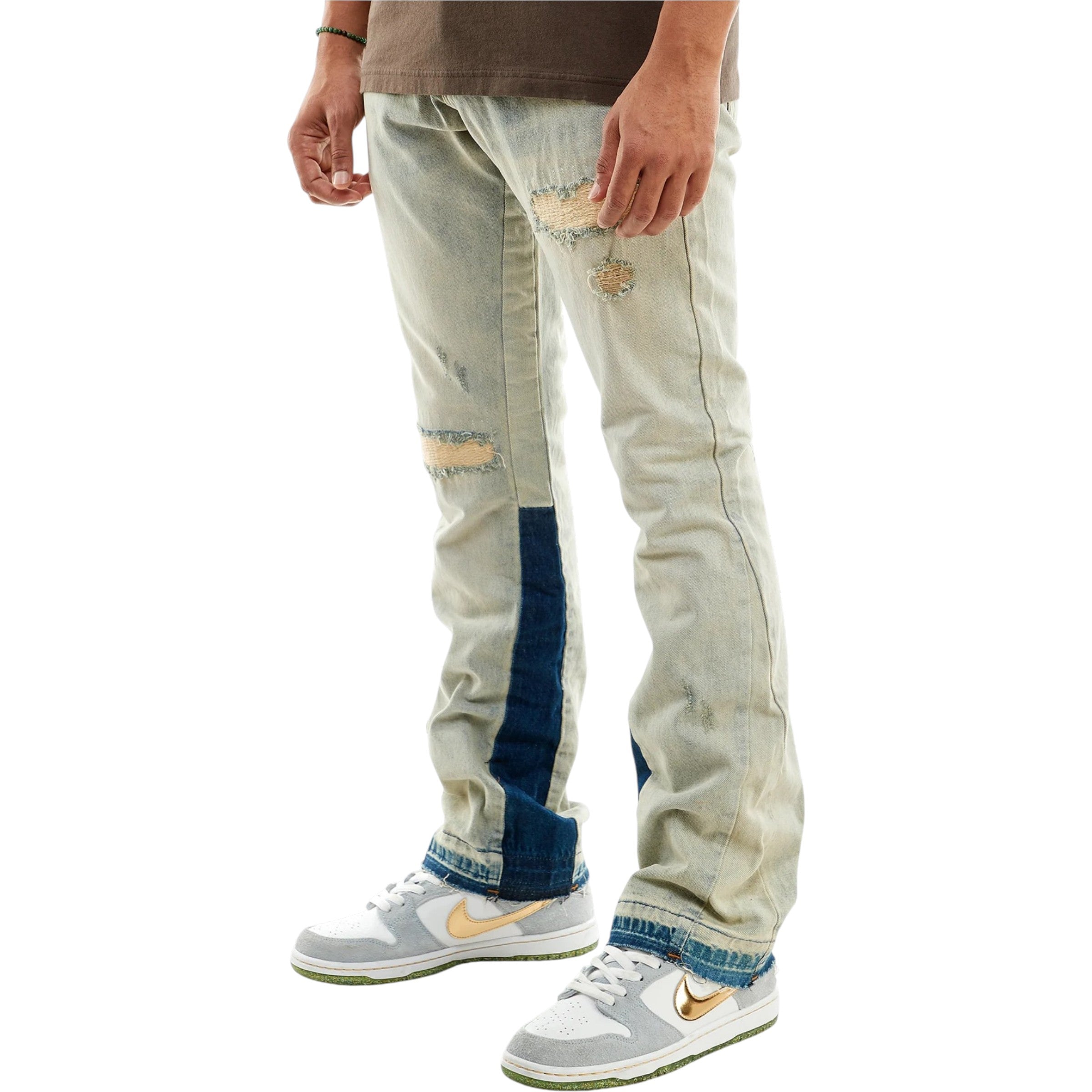 Light-colored distressed jeans with blue patches worn by a person, paired with white sneakers featuring a logo. stacked flared jeans